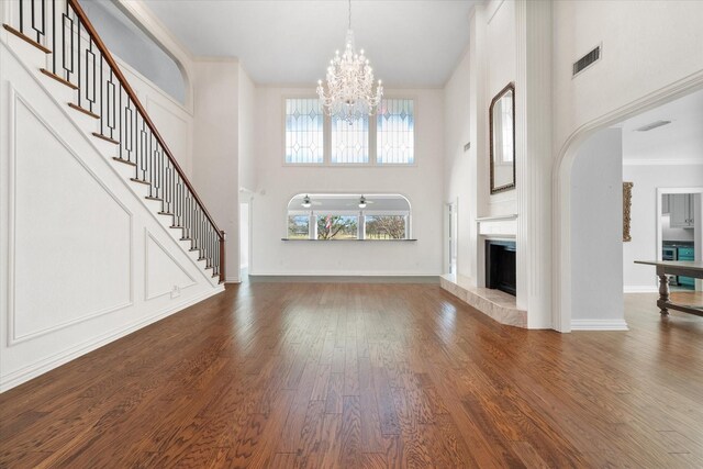 unfurnished living room featuring a fireplace, a high ceiling, a notable chandelier, and ornamental molding