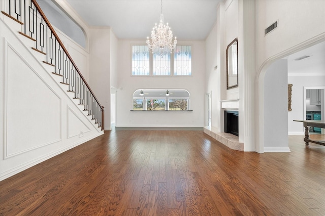 unfurnished living room featuring crown molding, hardwood / wood-style flooring, a tile fireplace, a high ceiling, and a notable chandelier