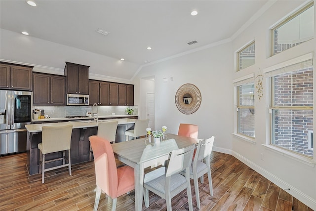 dining space featuring hardwood / wood-style flooring, vaulted ceiling, and ornamental molding