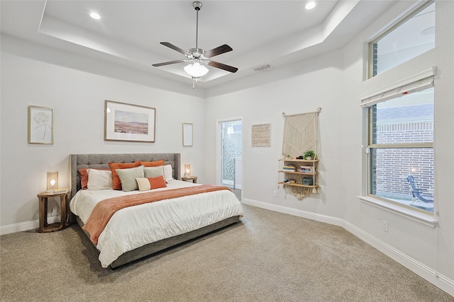 carpeted bedroom with multiple windows, a tray ceiling, and ceiling fan