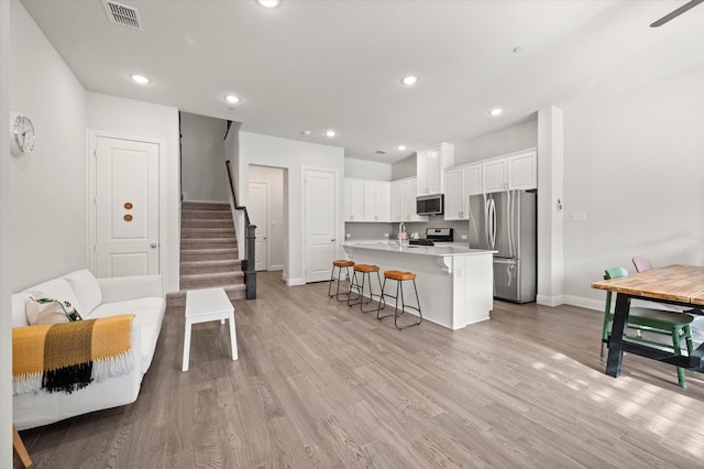 kitchen with light wood-type flooring, an island with sink, a kitchen bar, white cabinetry, and stainless steel appliances