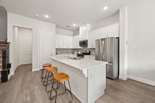 kitchen featuring decorative backsplash, appliances with stainless steel finishes, a kitchen breakfast bar, a center island with sink, and white cabinets