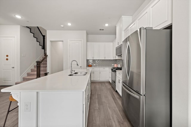 kitchen with sink, backsplash, an island with sink, white cabinets, and appliances with stainless steel finishes