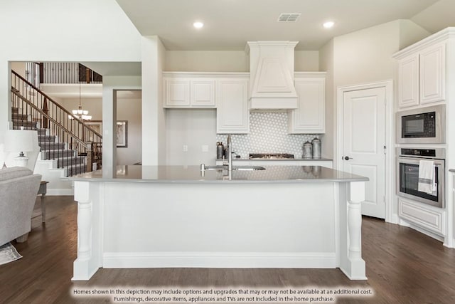 kitchen featuring stainless steel appliances, white cabinetry, custom range hood, and a kitchen island with sink