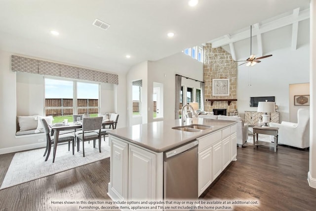 kitchen featuring a stone fireplace, an island with sink, sink, white cabinets, and stainless steel dishwasher