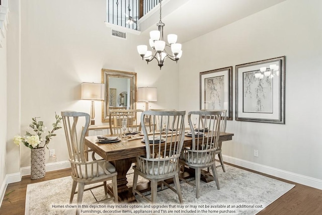 dining area with hardwood / wood-style flooring, a towering ceiling, and a notable chandelier