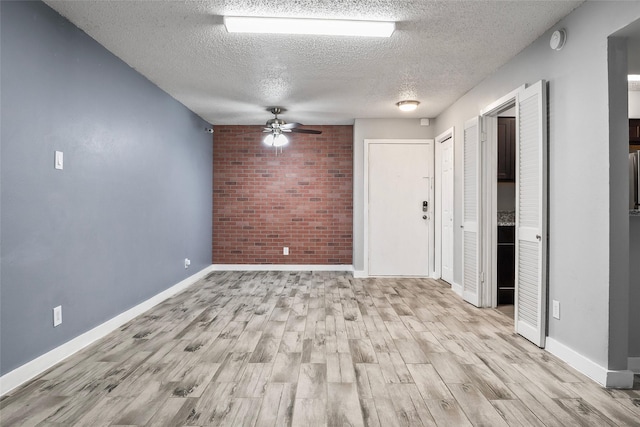 empty room featuring light wood-type flooring, a textured ceiling, ceiling fan, and brick wall