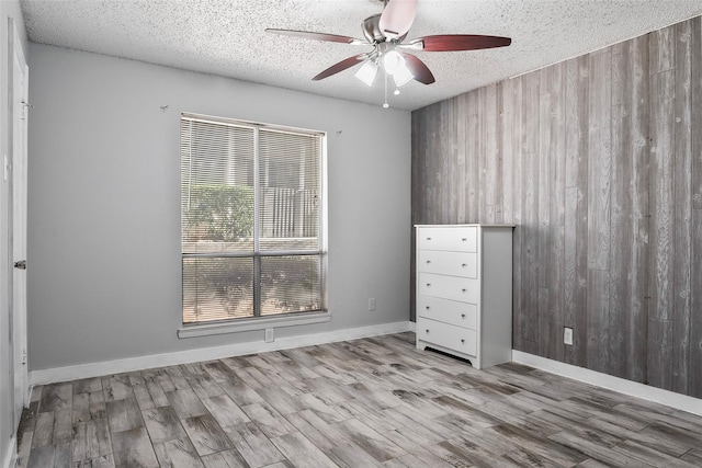 empty room with wooden walls, ceiling fan, light hardwood / wood-style floors, and a textured ceiling