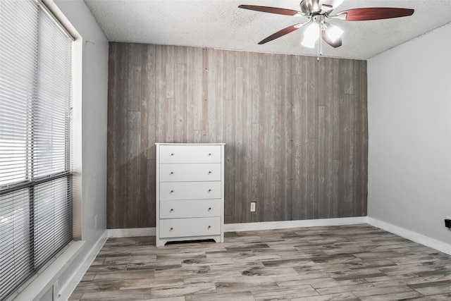 spare room with ceiling fan, wood walls, wood-type flooring, and a textured ceiling