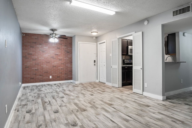 empty room with a textured ceiling, light hardwood / wood-style flooring, ceiling fan, and brick wall