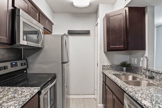 kitchen with light stone countertops, a textured ceiling, stainless steel appliances, dark brown cabinetry, and sink