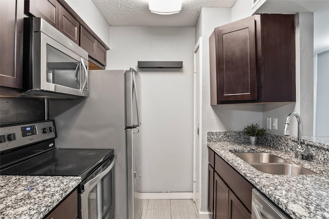 kitchen with light stone counters, sink, a textured ceiling, and appliances with stainless steel finishes