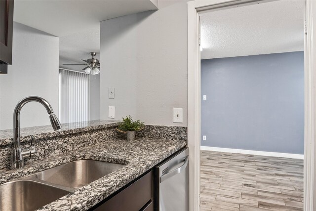 kitchen with light wood-type flooring, stainless steel dishwasher, dark stone counters, a textured ceiling, and sink