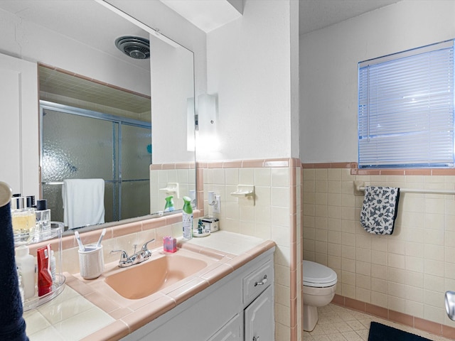 bathroom with vanity, a shower with door, tile patterned flooring, toilet, and tile walls