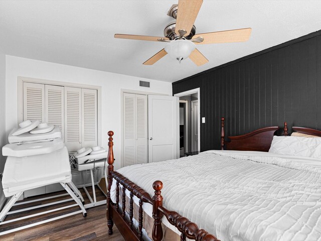 bedroom with dark hardwood / wood-style flooring, two closets, and ceiling fan