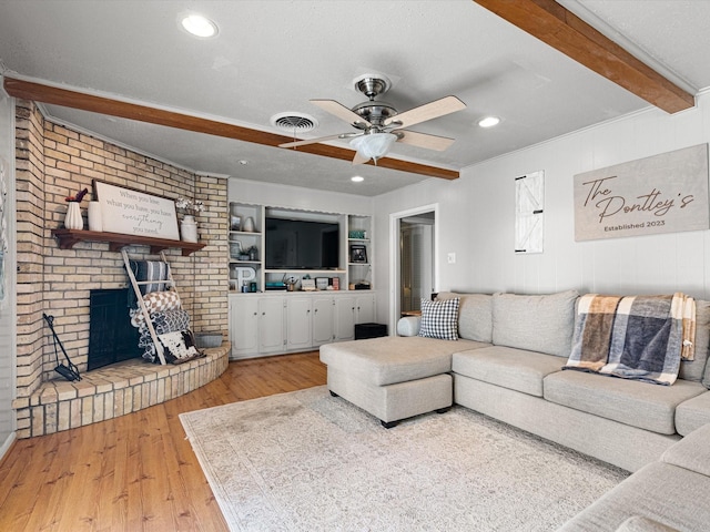 living room featuring a fireplace, beam ceiling, ceiling fan, a textured ceiling, and light wood-type flooring