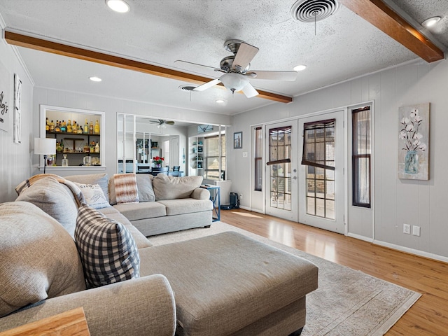 living room featuring french doors, ceiling fan, light wood-type flooring, a textured ceiling, and beam ceiling