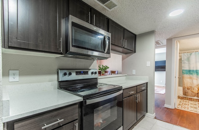 kitchen featuring light tile patterned floors, a textured ceiling, stainless steel appliances, and dark brown cabinetry