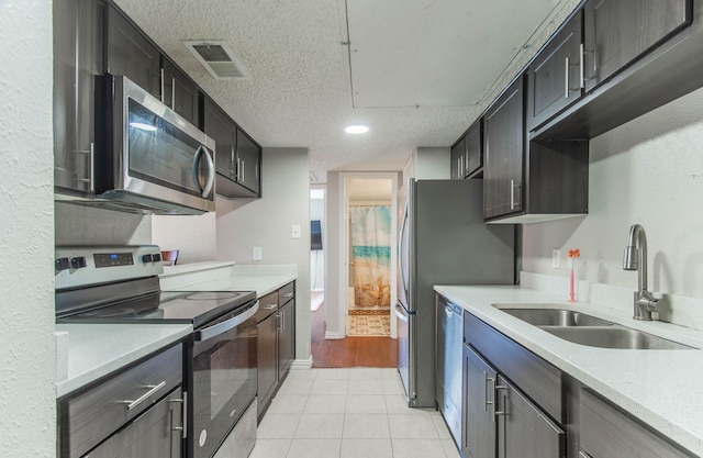 kitchen featuring a textured ceiling, sink, light tile patterned floors, and stainless steel appliances