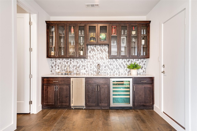 bar with sink, beverage cooler, dark hardwood / wood-style flooring, decorative backsplash, and dark brown cabinets