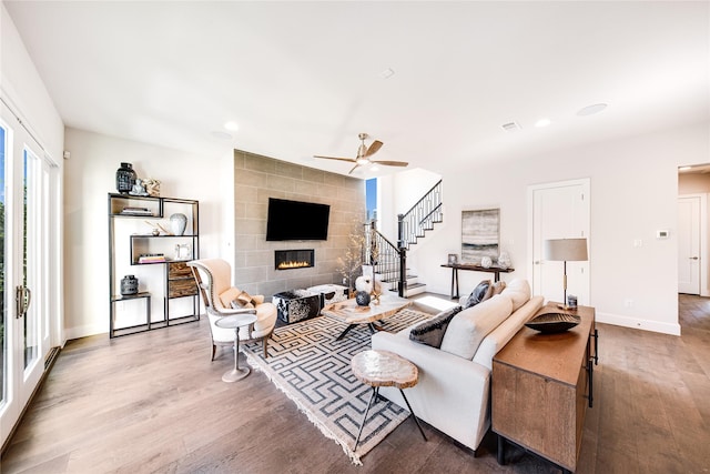 living room featuring a tile fireplace, ceiling fan, and wood-type flooring