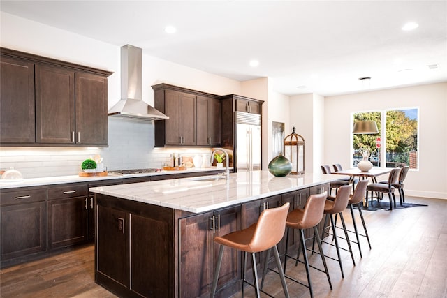 kitchen featuring sink, wall chimney exhaust hood, stainless steel appliances, dark hardwood / wood-style flooring, and an island with sink