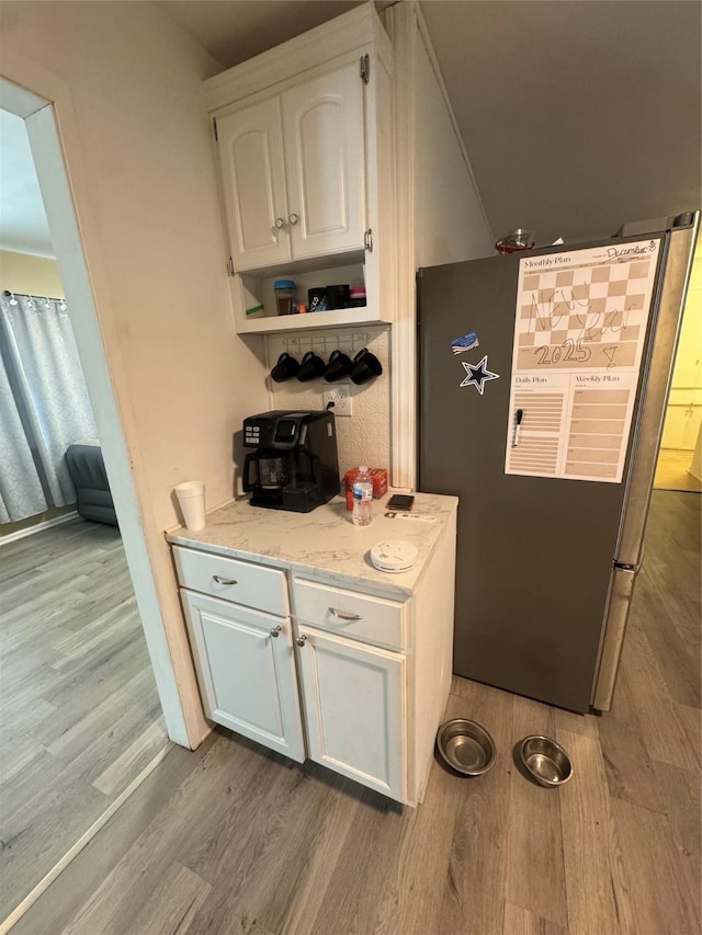 kitchen featuring light stone countertops, light hardwood / wood-style floors, stainless steel refrigerator, and white cabinets