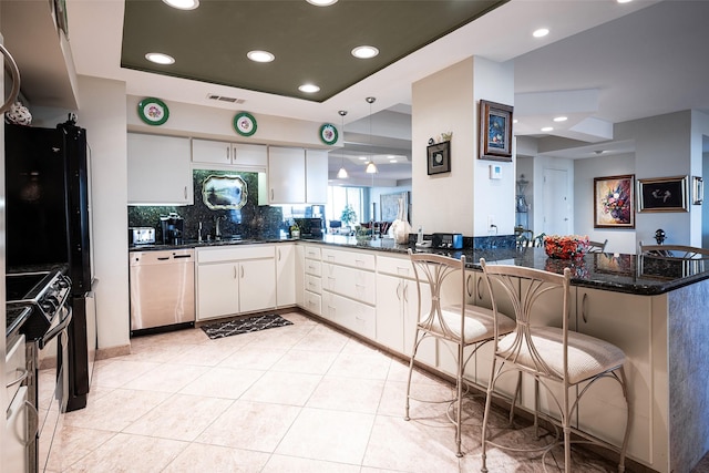 kitchen featuring stainless steel appliances, kitchen peninsula, dark stone counters, a kitchen bar, and white cabinets