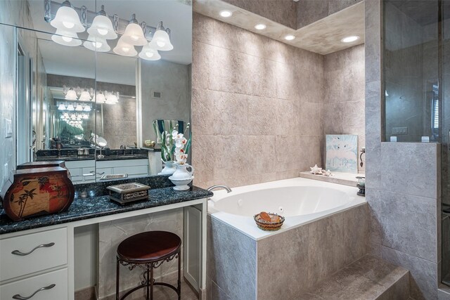 bathroom featuring tiled tub, vanity, and tile walls