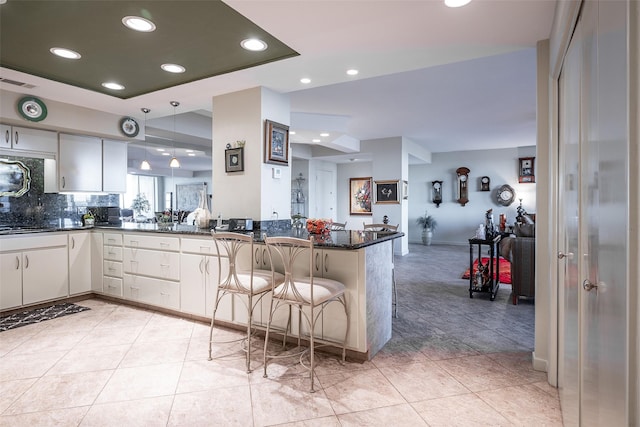 kitchen with a breakfast bar area, dark stone countertops, kitchen peninsula, pendant lighting, and decorative backsplash