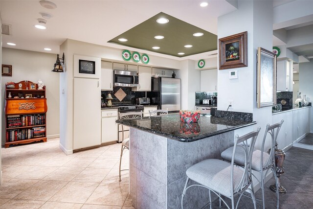 kitchen with a kitchen breakfast bar, decorative backsplash, dark stone countertops, white cabinetry, and stainless steel appliances