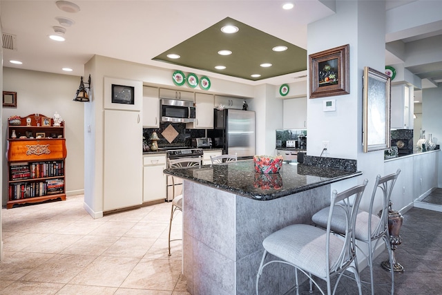 kitchen with appliances with stainless steel finishes, dark stone countertops, tasteful backsplash, white cabinets, and a kitchen bar