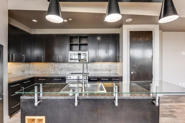 kitchen with a center island with sink, hanging light fixtures, and dark stone counters