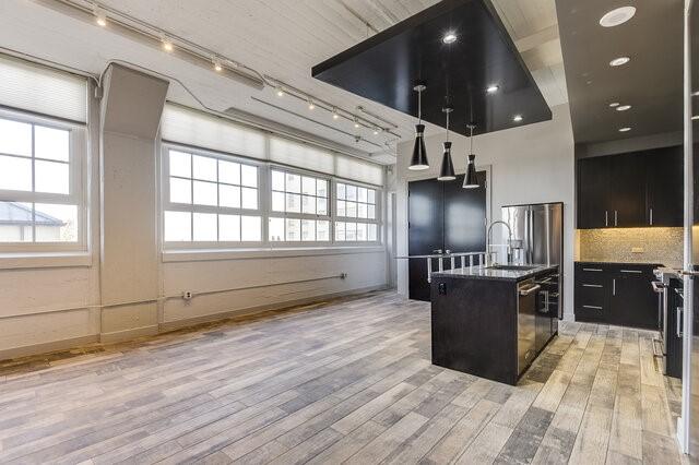 kitchen with decorative backsplash, sink, light hardwood / wood-style flooring, hanging light fixtures, and an island with sink