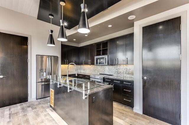 kitchen featuring pendant lighting, a center island with sink, decorative backsplash, light wood-type flooring, and appliances with stainless steel finishes