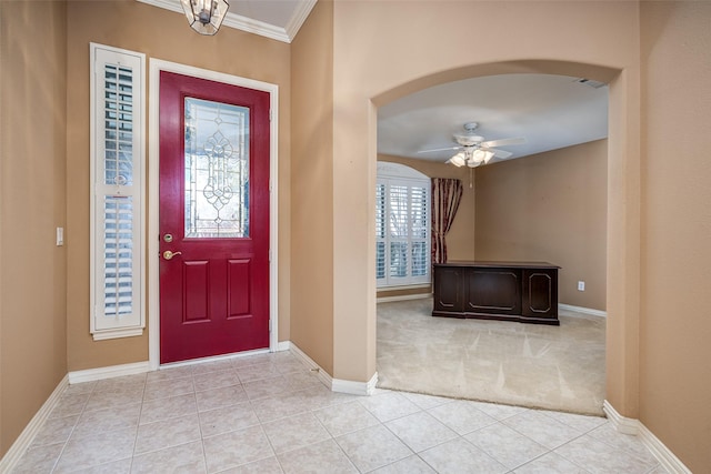 entrance foyer featuring arched walkways, ceiling fan, light tile patterned flooring, and crown molding