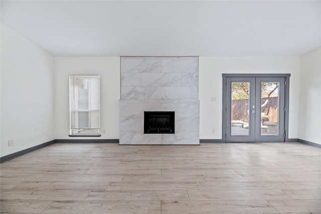 unfurnished living room with light wood-type flooring, a premium fireplace, and french doors