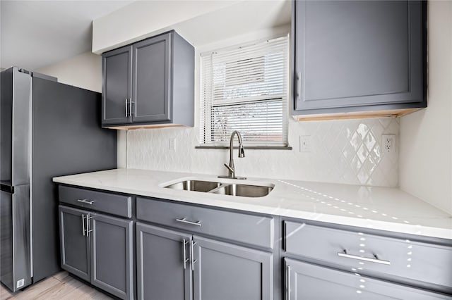 kitchen with gray cabinetry, sink, stainless steel fridge, light wood-type flooring, and light stone countertops