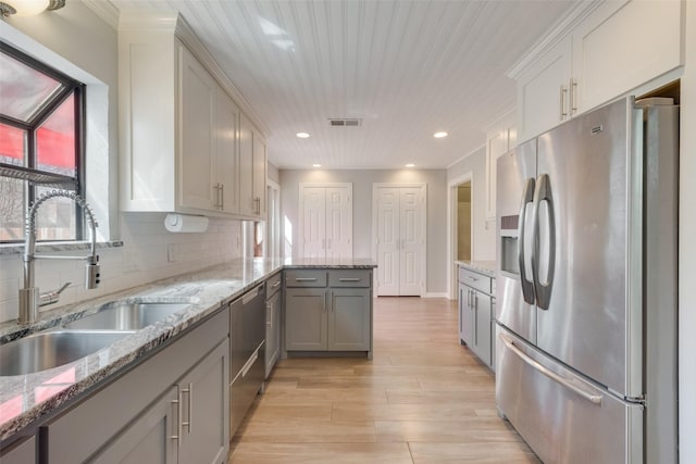 kitchen with light stone counters, a sink, backsplash, appliances with stainless steel finishes, and a peninsula