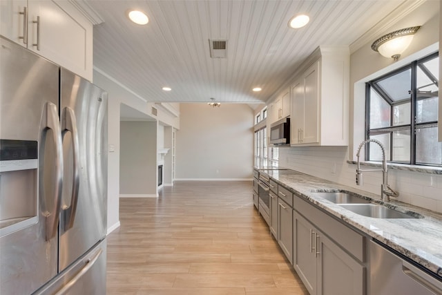 kitchen with decorative backsplash, light wood-style flooring, appliances with stainless steel finishes, a sink, and light stone counters