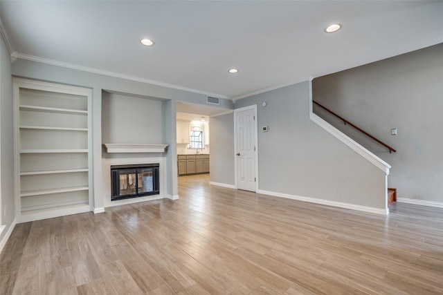 unfurnished living room featuring crown molding, built in features, and light wood-type flooring