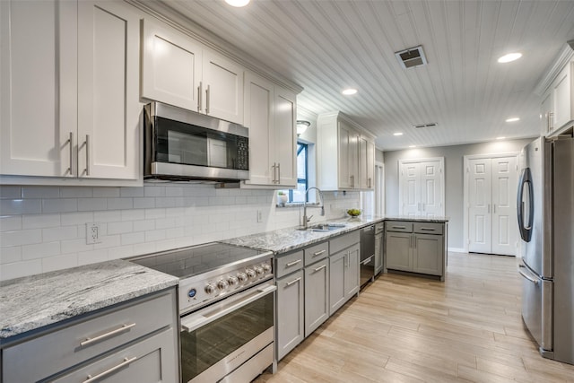 kitchen with light stone countertops, gray cabinetry, stainless steel appliances, sink, and light hardwood / wood-style flooring