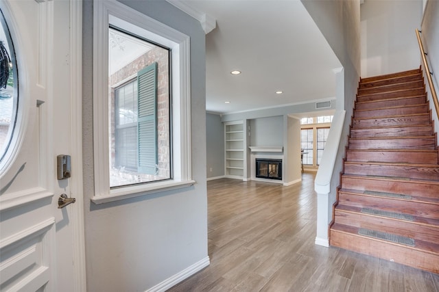 entrance foyer with recessed lighting, stairway, a glass covered fireplace, light wood-type flooring, and baseboards