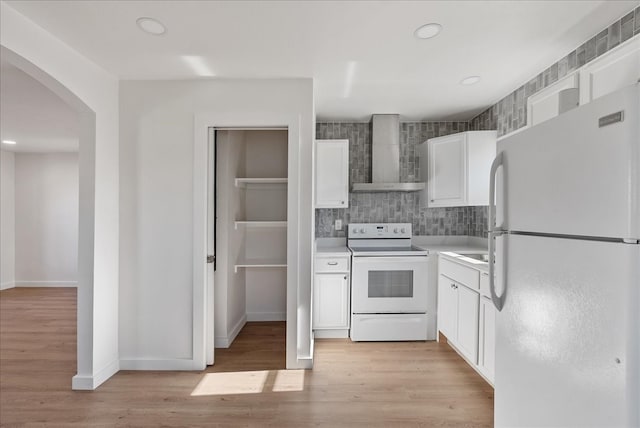 kitchen featuring backsplash, white cabinets, white appliances, light wood-type flooring, and wall chimney exhaust hood