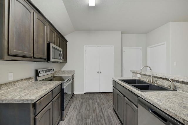 kitchen featuring dark brown cabinetry, lofted ceiling, sink, appliances with stainless steel finishes, and dark hardwood / wood-style flooring