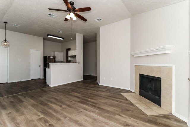 unfurnished living room with ceiling fan, a fireplace, dark wood-type flooring, and a textured ceiling