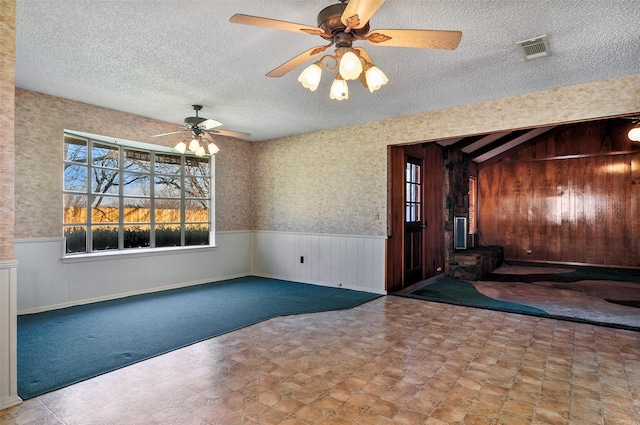 unfurnished room with ceiling fan, wood walls, a wood stove, and a textured ceiling