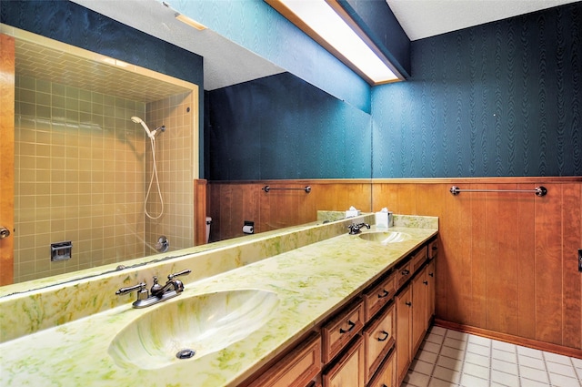 bathroom with tile patterned flooring, a tile shower, vanity, and wood walls