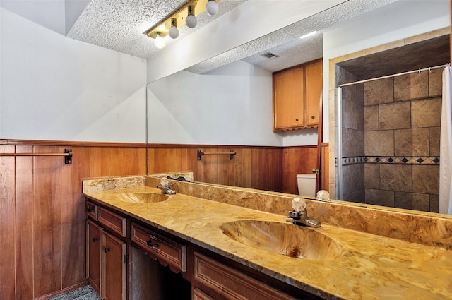 bathroom featuring vanity, wood walls, a shower with shower curtain, toilet, and a textured ceiling