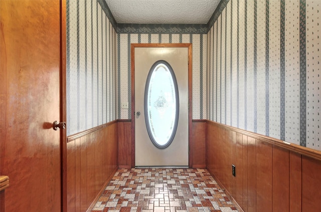 doorway to outside featuring a textured ceiling and wood walls